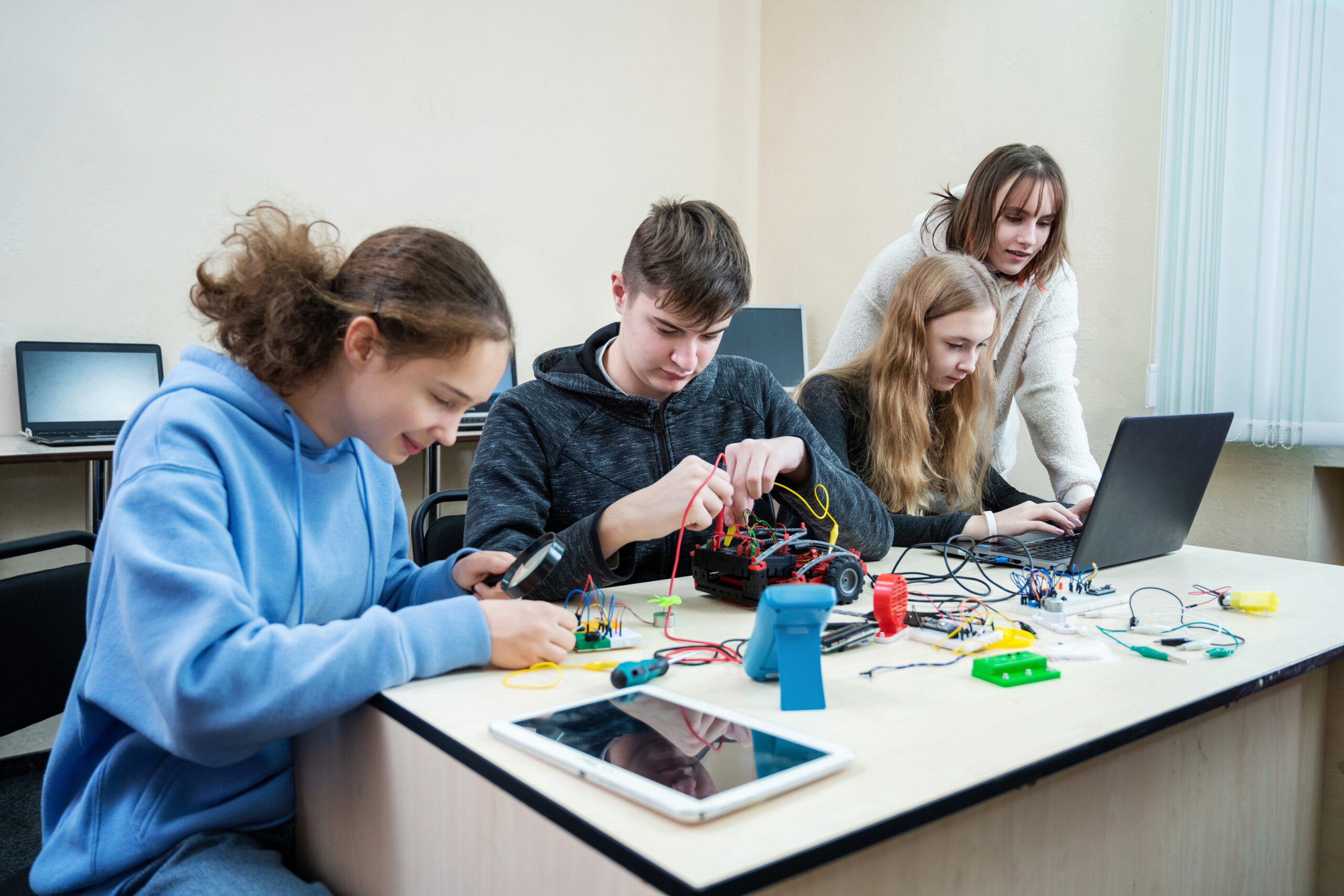 Diverse teenager pupils build robot vehicle learning at table at STEM engineering science education class.